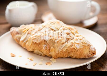 Un bon croissant aux amandes sur une assiette blanche servi avec une tasse de café et de crème. Vue en gros plan Banque D'Images