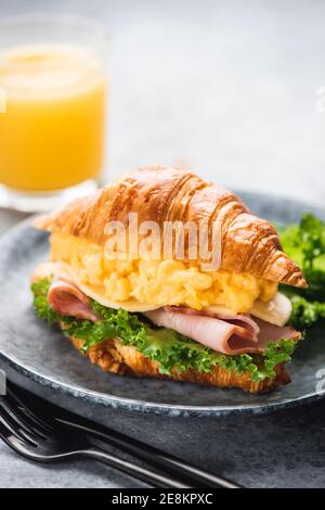Petit-déjeuner croissant avec jambon de dinde, œufs brouillés, fromage et salade de laitue servis avec un verre de jus d'orange frais. Brea de style continental Banque D'Images