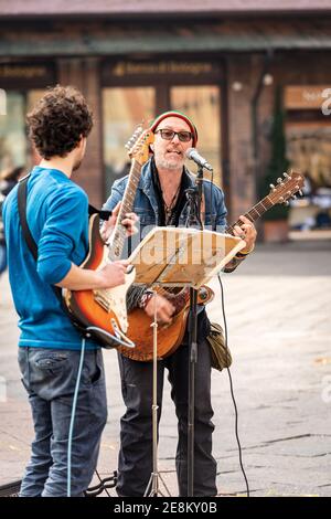 Deux musiciens de rue non identifiés jouent de la guitare et chantent pour divertir les gens qui marchent sur la Piazza Maggiore, au centre-ville de Bologne, en Emilie-Romagne, en Italie. Banque D'Images