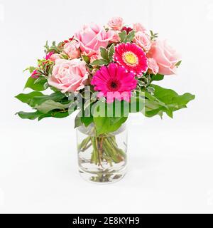 Un joli bouquet de roses et de gerberas dans un vase en verre, isolé sur un sol blanc Banque D'Images