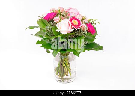 Un joli bouquet de roses et de gerberas dans un vase en verre, isolé sur un sol blanc Banque D'Images