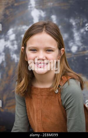 Jeune fille dans une robe générale brune en hiver assis près d'un mur d'entrepôt urbain Banque D'Images