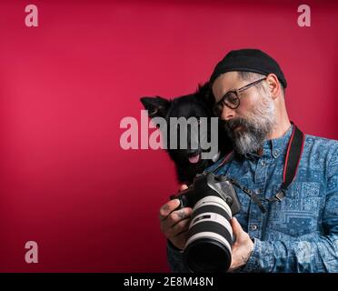 Homme regardant des photos de l'appareil photo avec son chien dans un studio sur fond rouge Banque D'Images