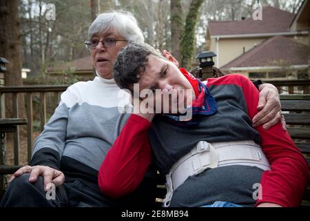 Jonesboro, GA, États-Unis. 31 janvier 2021. Sheila McBroom réconforte son fils Tim handicapé en s'asseyent sur la terrasse familiale. McBroom et son mari Mike sont souvent éveillés la nuit, remplis d'inquiétude quant à l'avenir de Tim's. Tim, 36 ans, qui est non verbal et connaît un autisme grave, a des crises et des problèmes de comportement. McBroom et sa femme font de leur mieux pour offrir à leur fils un environnement sûr et sécuritaire dans leur maison de Jonesboro, avec l'aide quotidienne du personnel de soutien financé par Medicaid. Mais les réductions proposées à ces services financés par Medicaid bouleversent la vie de leur fils s. Georgia's disab Banque D'Images