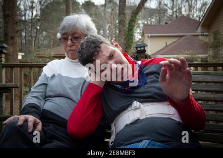 Jonesboro, GA, États-Unis. 31 janvier 2021. Sheila McBroom réconforte son fils Tim handicapé en s'asseyent sur la terrasse familiale. McBroom et son mari Mike sont souvent éveillés la nuit, remplis d'inquiétude quant à l'avenir de Tim's. Tim, 36 ans, qui est non verbal et connaît un autisme grave, a des crises et des problèmes de comportement. McBroom et sa femme font de leur mieux pour offrir à leur fils un environnement sûr et sécuritaire dans leur maison de Jonesboro, avec l'aide quotidienne du personnel de soutien financé par Medicaid. Mais les réductions proposées à ces services financés par Medicaid bouleversent la vie de leur fils s. Georgia's disab Banque D'Images