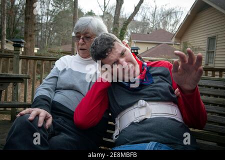 Jonesboro, GA, États-Unis. 31 janvier 2021. Sheila McBroom réconforte son fils Tim handicapé en s'asseyent sur la terrasse familiale. McBroom et son mari Mike sont souvent éveillés la nuit, remplis d'inquiétude quant à l'avenir de Tim's. Tim, 36 ans, qui est non verbal et connaît un autisme grave, a des crises et des problèmes de comportement. McBroom et sa femme font de leur mieux pour offrir à leur fils un environnement sûr et sécuritaire dans leur maison de Jonesboro, avec l'aide quotidienne du personnel de soutien financé par Medicaid. Mais les réductions proposées à ces services financés par Medicaid bouleversent la vie de leur fils s. Georgia's disab Banque D'Images