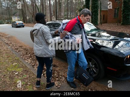 Jonesboro, GA, États-Unis. 31 janvier 2021. Un personnel de soutien financé par Medicaid escorte Tim McBroom à sa voiture pour un trajet en ville comme activité de l'après-midi. Mike et Sheila McBroom sont souvent éveillés la nuit, remplis d'anxiété au sujet de leur fils adultes handicapés, Tim's future. Tim, 36 ans, qui est non verbal et connaît un autisme grave, a des crises et des problèmes de comportement. McBroom et sa femme font de leur mieux pour offrir à leur fils un environnement sûr et sécuritaire dans leur maison de Jonesboro, avec l'aide quotidienne du personnel de soutien financé par Medicaid. Mais a proposé des réductions de ces services financés par Medicaid Banque D'Images