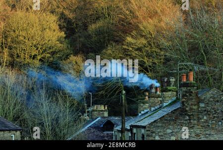 Les derniers rayons du soleil d'hiver mettent en évidence les arbres et la vue bienvenue d'une cheminée de chalet de tabac indique une maison chaude venant pour certains. Banque D'Images