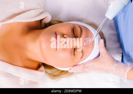 Femme âgée avec bandeau blanc recevant un massage facial électrique de darsonval au salon de beauté. Vue ci-dessus Banque D'Images