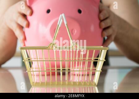 l'homme a une grande banque de porc dans ses mains, un panier doré se tient sur la table en face d'eux. Le concept de l'économie Banque D'Images