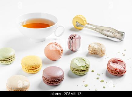 Délicieux macarons français multicolores ou macarons dans un mess et une tasse de thé sur une table blanche Banque D'Images