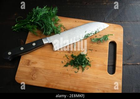 Hacher de l'aneth frais sur une planche à découper en bambou : hacher des lanières d'aneth frais sur une planche à découper en bois avec un couteau de chef Banque D'Images