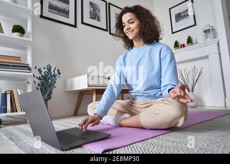 Bonne bonne tenue jeune femme utilisant un ordinateur portable regardant la leçon de yoga en ligne à la maison. Banque D'Images