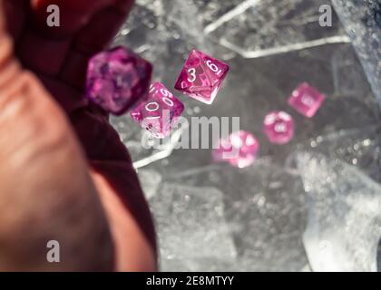 Jeu de rôle rose dés de jeu tombant d'un main sur des feuilles de glace sous le soleil d'hiver Banque D'Images