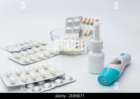 Des cloques et des comprimés d'argentée, une bouteille de vaporisateur nasal et un thermomètre électronique se trouvent sur un fond blanc. Banque D'Images