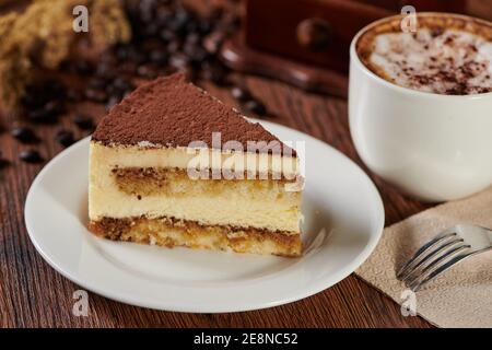 Une tranche de gâteau de tiramisu sur une assiette avec un cappuccino sur une table en bois Banque D'Images