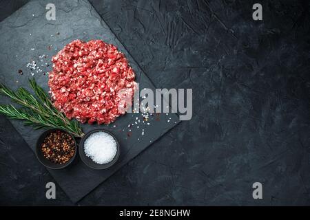 Viande hachée, sel, épices et romarin sur un plateau plat sur fond noir. Banque D'Images