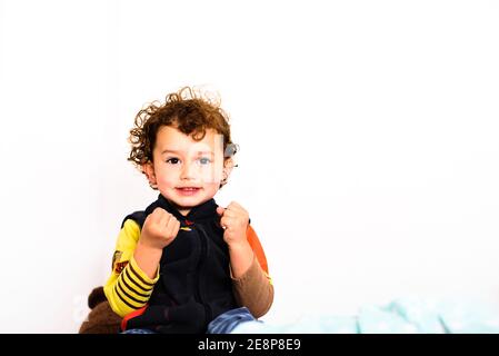 Petite fille dans sa chambre souriant heureusement, empaquemmenée un jour d'hiver, isolée sur blanc. Banque D'Images