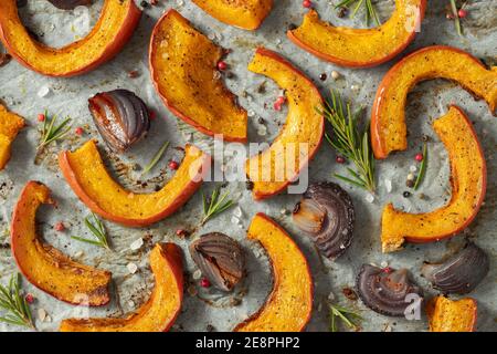 Gros plan de citrouille rôtie avec ajout d'herbes aromatiques, d'oignon rouge, de sel de mer et d'huile d'olive. Fond d'automne de citrouille. Vue de dessus Banque D'Images