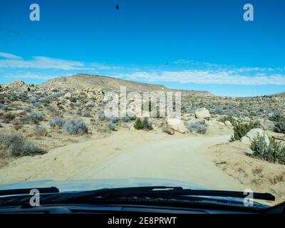 Vue à travers le pare-brise sur la route du désert de terre avec yuccas, ciel bleu, soleil dans la vallée de Yucca Californie près du parc national de Joshua Tree et Rimrock Banque D'Images