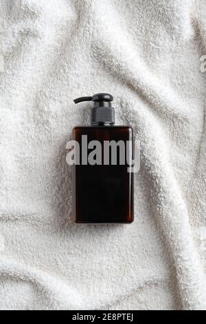 Bouteille de shampoing à pompe en verre ambré sur une serviette blanche dans la salle de bains. SPA cosmétiques naturels bio design d'emballage. Flat lay, vue de dessus. Banque D'Images