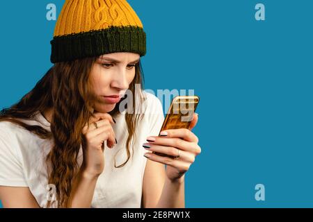 Femme effectuant un appel vidéo à l'aide d'un téléphone isolé sur fond bleu. Portrait de surprise bouleversé triste esprit de femme regardant le téléphone essayer à und Banque D'Images