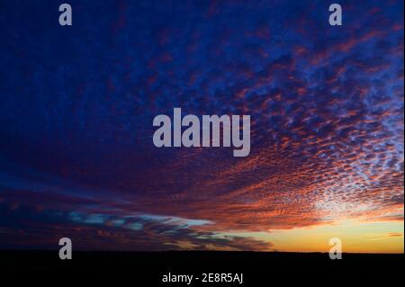 Sous des nuages éclairés révélant un ciel bleu profond et un coucher de soleil enflammé. Banque D'Images