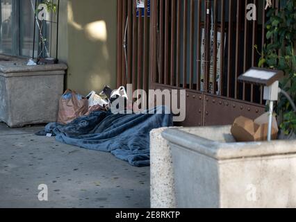 Los Angeles, CA USA - le 9 janvier 2021 : un homme sans abri qui dort sur le trottoir devant ou un restaurant qui a été fermé par la quarantaine du coronavirus Banque D'Images