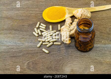 Capsules de plantes de curcuma en bouteille noire, racine de curcuma fraîche et poudre de curcuma dans une cuillère en bois sur fond en bois Banque D'Images