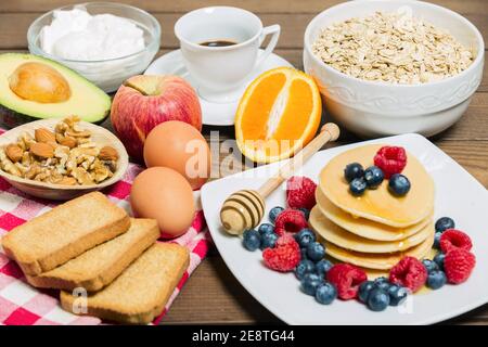 Un petit déjeuner sain avec du café, des crêpes, des baies fraîches, des œufs, de l'avocat, du yaourt grec, de l'avoine, des roussettes et de l'orange. Banque D'Images