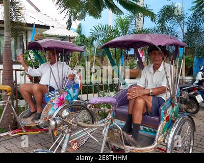 Deux hommes pilotes de pédiab s'assoient à la légère dans leurs rickshaws en attendant pour l'arrivée des passagers qui utiliseront leurs services Banque D'Images