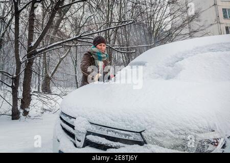 Une jeune fille nettoie sa voiture de la neige après une chute de neige Banque D'Images