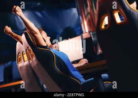 Gagnant. Vue latérale d'une jeune joueuse de cybersport excitée qui se relève, célébrant le succès tout en jouant à des jeux vidéo en ligne professionnellement, le tournoi eSport Banque D'Images