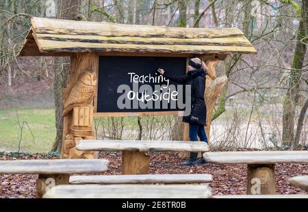 Une enseignante écrit sur un tableau noir « enseigner à l'extérieur ». Une salle de classe dans la forêt est qualifiée pour enseigner pendant la pandémie de corona. Banque D'Images