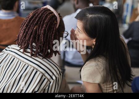 Vue en grand angle de deux femmes qui chuchotent tout en étant assise dans le public lors d'une conférence d'affaires ou d'un séminaire, espace de copie Banque D'Images