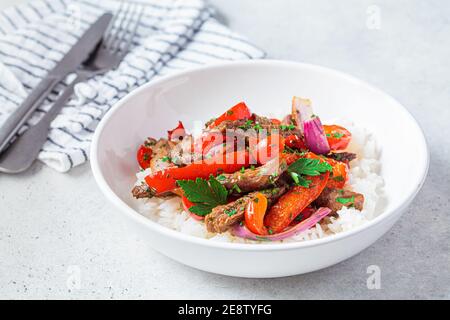 Morceaux de bœuf frits avec légumes et riz dans une assiette blanche. Faire sauter le bœuf avec les poivrons et les oignons, servi avec le riz. Banque D'Images