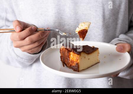 Femme méconnaissable mangeant une tranche d'un basque traditionnel brûlé cheesecake Banque D'Images