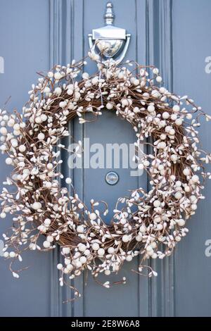 Gros plan : magnifique décoration de couronne de Noël avec branches brunes et baies de GUI blanches suspendues sur la porte avant bleue. Style anglais maison. Banque D'Images