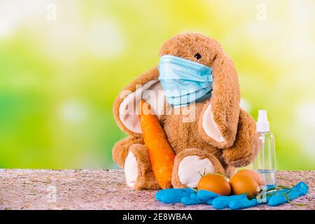 Lapin sur fond vert avec masque pour coronavirus, œufs, grosse carotte, gants de protection et désinfectant autour de la composition. Joyeuses pâques et Banque D'Images