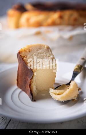 Gros plan de la portion mordue du gâteau au fromage basque brûlé sur une assiette blanche avec une cuillère vintage sur le côté. Cheesecake non concentré à l'arrière-plan. Espagnol fait maison Banque D'Images