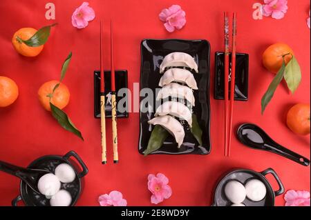 Nouvel an chinois nourriture et boisson encore vie. Boulettes vapeur, boulettes de riz Tangyuan, biscuits fortune sur plaque noire et fond rouge. Photo de haute qualité. Ci-dessus Banque D'Images