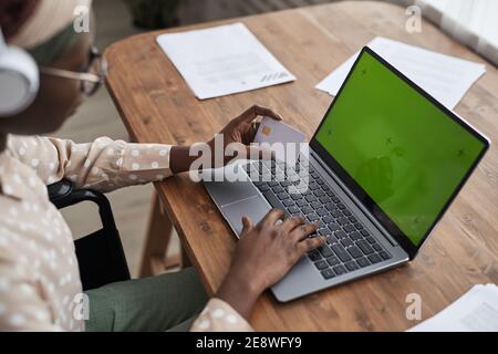 Gros plan à grand angle de la femme afro-américaine dans les achats en ligne en fauteuil roulant via ordinateur portable et tenant la carte de crédit à l'écran vert, copie spac Banque D'Images