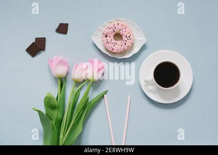 Beignet rose sur soucoupe, tulipes roses et café sur fond bleu. Petit déjeuner romantique pour la Saint-Valentin au lit pour l'être aimé. Le concept de m Banque D'Images