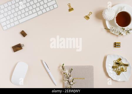 Espace de travail féminin avec ordinateur portable, tasse de thé, guimauve et fleurs sur table beige. Maquette de la vue de dessus.