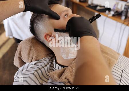 coiffeur habile. Un jeune homme se rasez à l'ancienne avec un rasoir droit. Banque D'Images