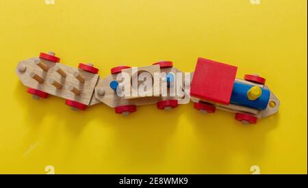 Jouet pour enfants en train, jeu pour enfants d'âge préscolaire. Locomotive et voitures, construction de blocs en bois colorés sur fond jaune, vue de dessus Banque D'Images