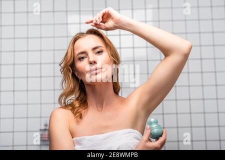 femme dans une serviette blanche appliquant un rouleau déodorant dans la salle de bains Banque D'Images