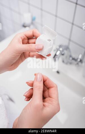 vue rognée d'une femme tenant un contenant en plastique avec un fil dentaire dans la salle de bains Banque D'Images