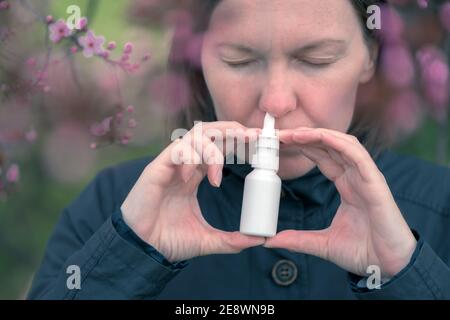 Femme utilisant un jet nasal à l'extérieur pour le traitement d'allergie au pollen d'arbre Banque D'Images