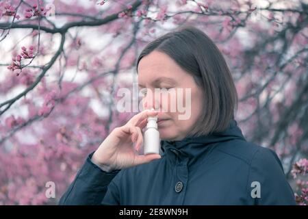 Femme utilisant un jet nasal à l'extérieur pour le traitement d'allergie au pollen d'arbre Banque D'Images